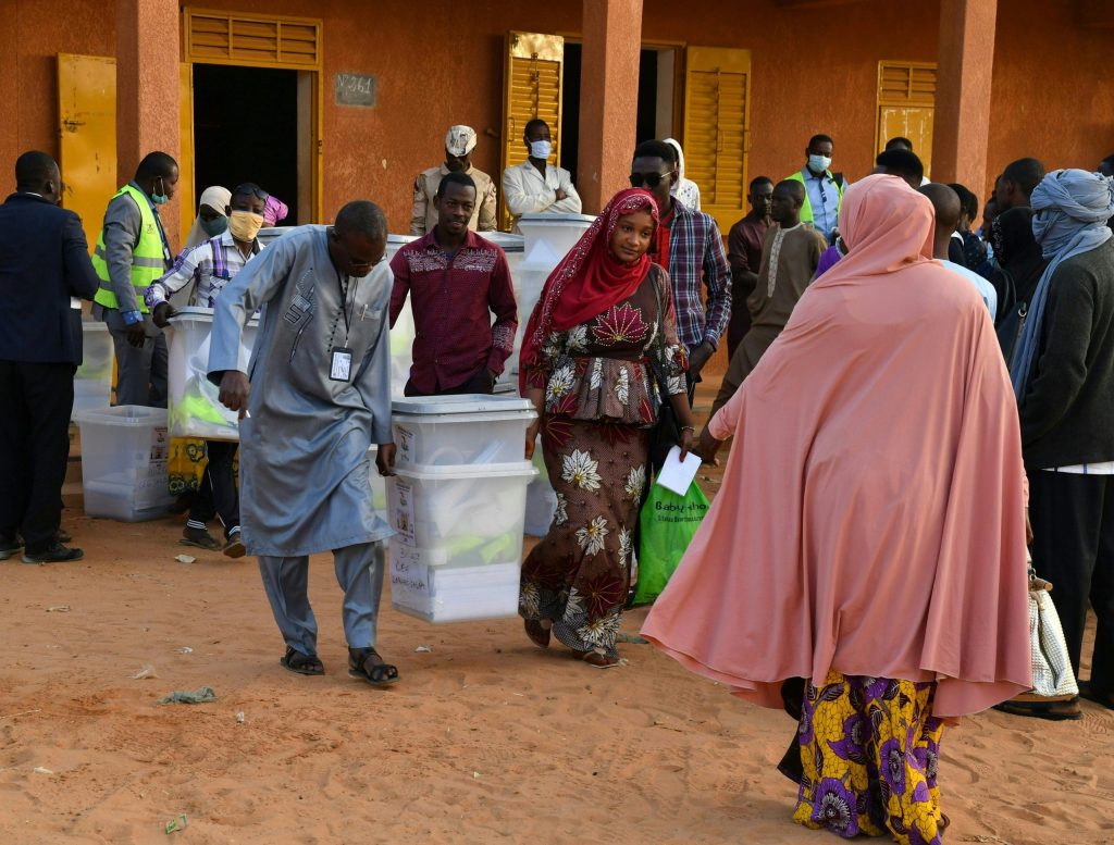 Des responsables de la commission électorale transportent des urnes devant un bureau de vote à Niamey le 27 décembre 2020 lors des élections présidentielles et législatives au Niger. - Les électeurs de l'État sahélien du Niger se rendent aux urnes le 27 décembre 2020 pour une élection qui pourrait sceller la toute première passation de pouvoir pacifique du pays entre les présidents élus, malgré une insurrection djihadiste sanglante. (Photo par Souleymane AG ANARA / AFP)